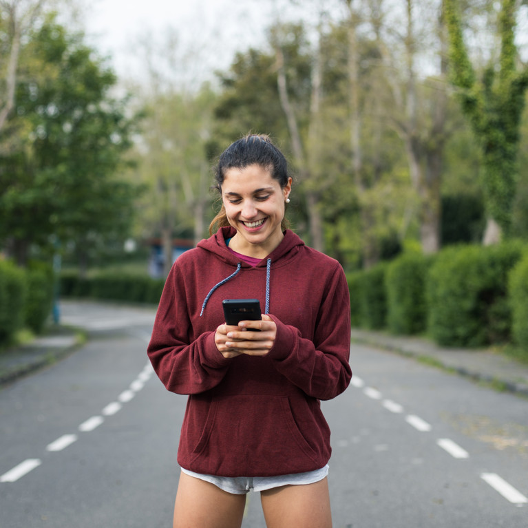 Sporty cheerful young woman taking a running rest for checking workout goals on smartphone app. Picture: Dirima/Adobe Stock
