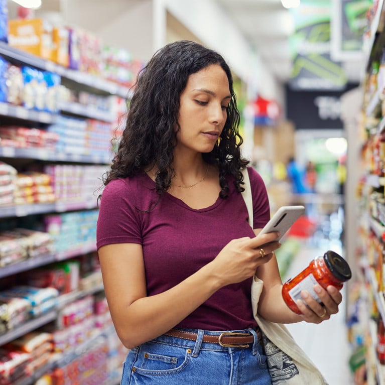Woman scanning a food jar label with her phone in a supermarket aisle