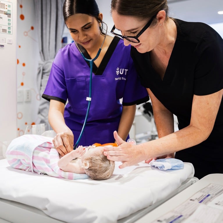 Two female health care university students training with a dummy baby.