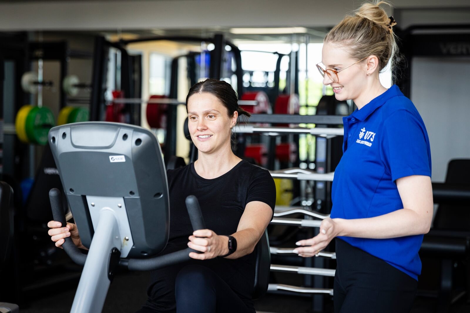 A clinical exercise physiologist assisting their client in a gym.