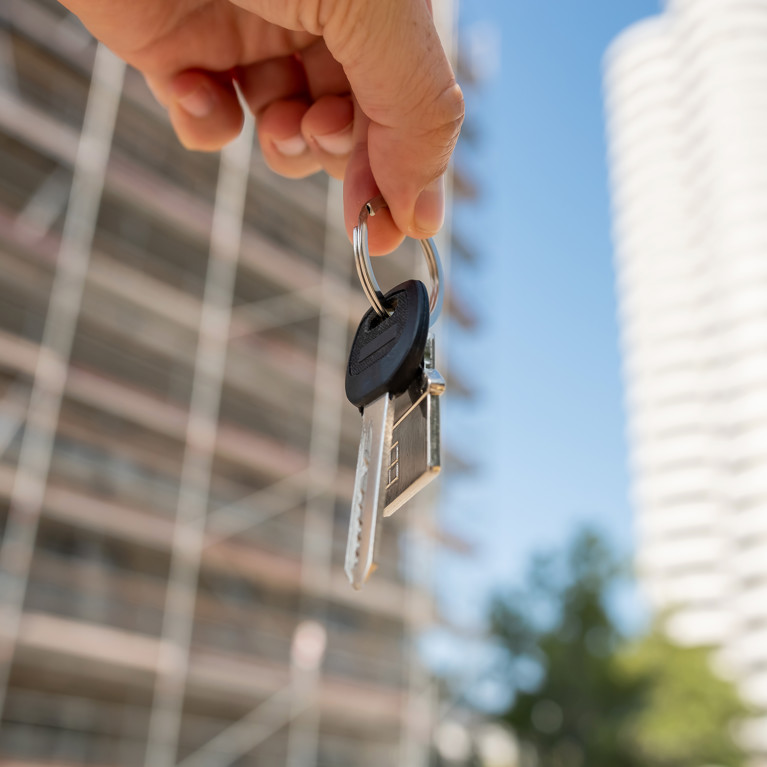 Female hand holding a set of keys outside, against new building. Picture by RomanR/Adobe Stock