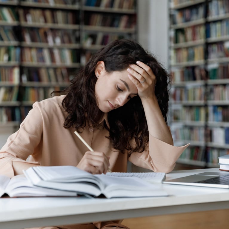 A young female student overloaded with study using her laptop, books and notes