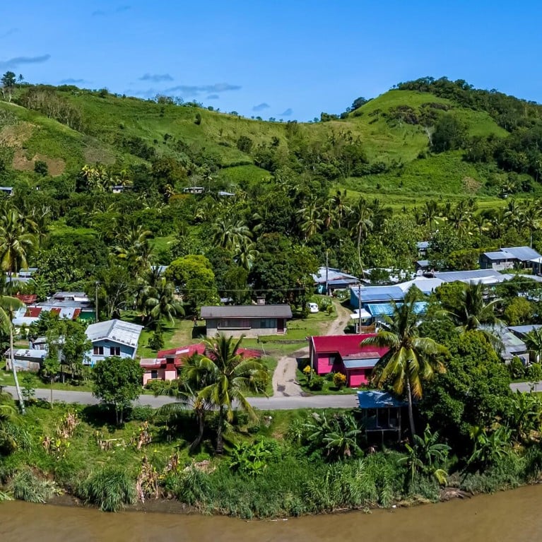 Aerial view of a Fijian village with houses nestled amongst palm trees on the banks of the Sigatoka River.