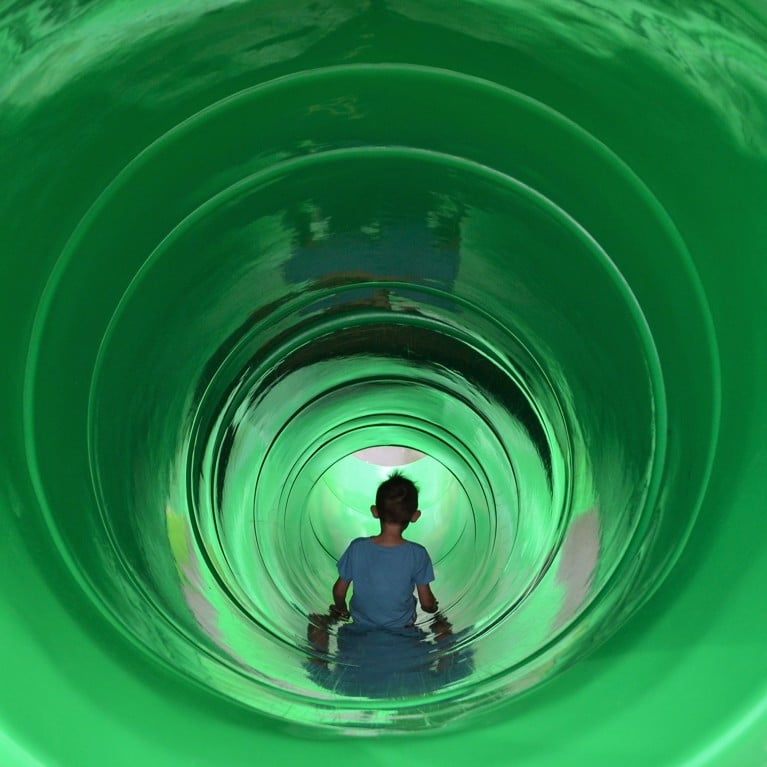 Boy sliding in a large green tunnel slide tube slide on a playground. Picture by PaulSat/Adobe Stock