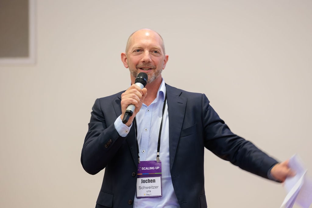 Jochen holding a microphone to his mouth with his left arm outstretched
