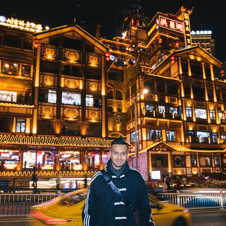 Sai stands in front of buildings at night in Asia