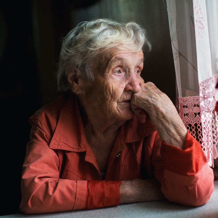 Older woman on her own staring out a window.