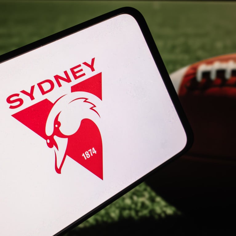 Sydney Swans team logo on phone screen with ball on the field background.
Picture: Ployker/Adobe Stock