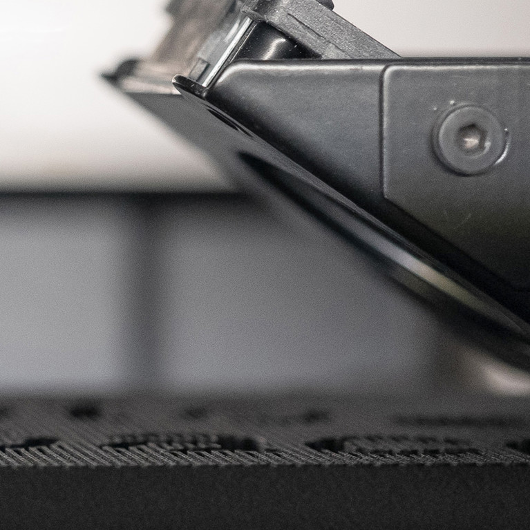 3D print head and black plastic part in focus showing material deposition and printing in process