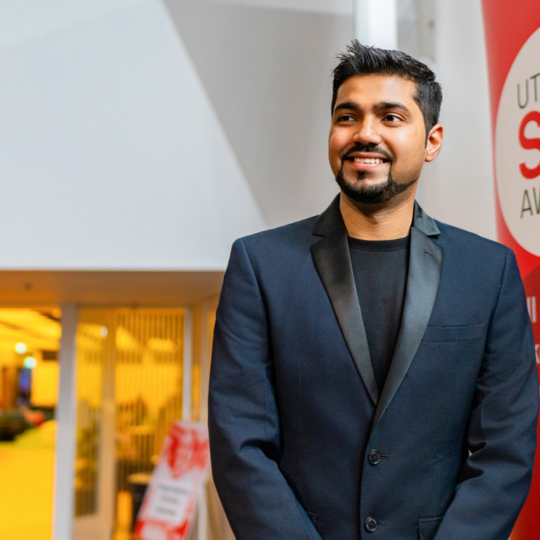 Shiva Sharma standing in front of a UTS SOUL Award banner looking to the left of the camera