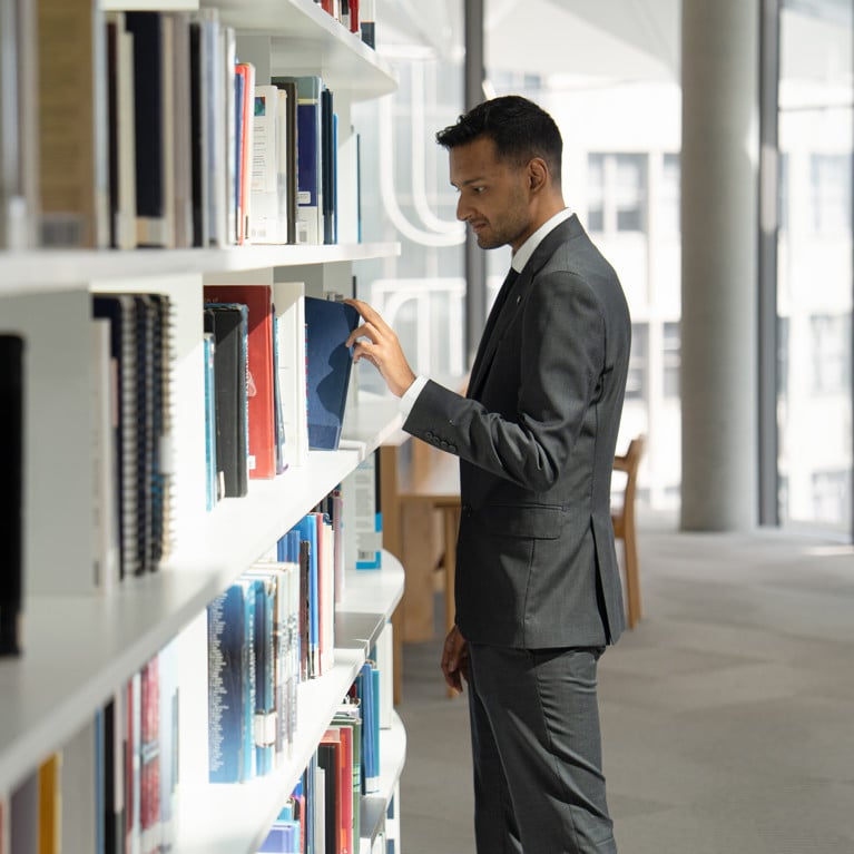 Sai browses in the UTS library, taking a blue book off the shelf
