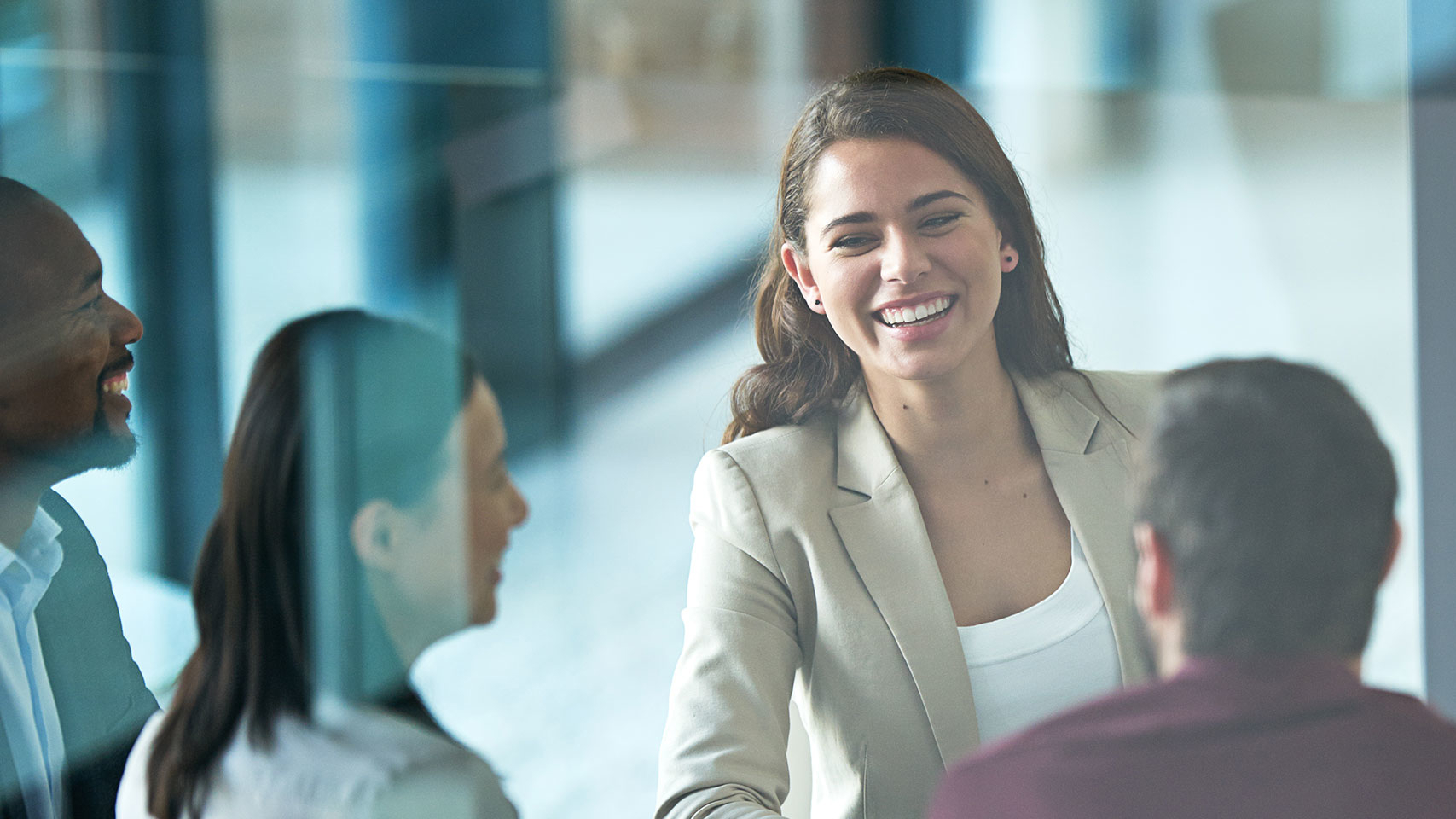 A woman smiles as she stands from a meeting table at which another woman and two men are seated.