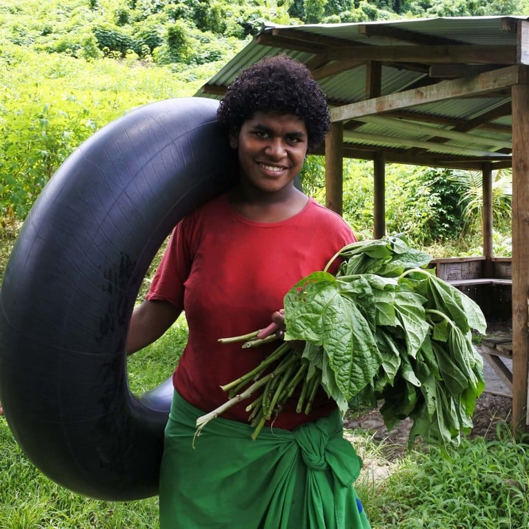 Smiling Fijian woman holding plants and an inflatable tyre.