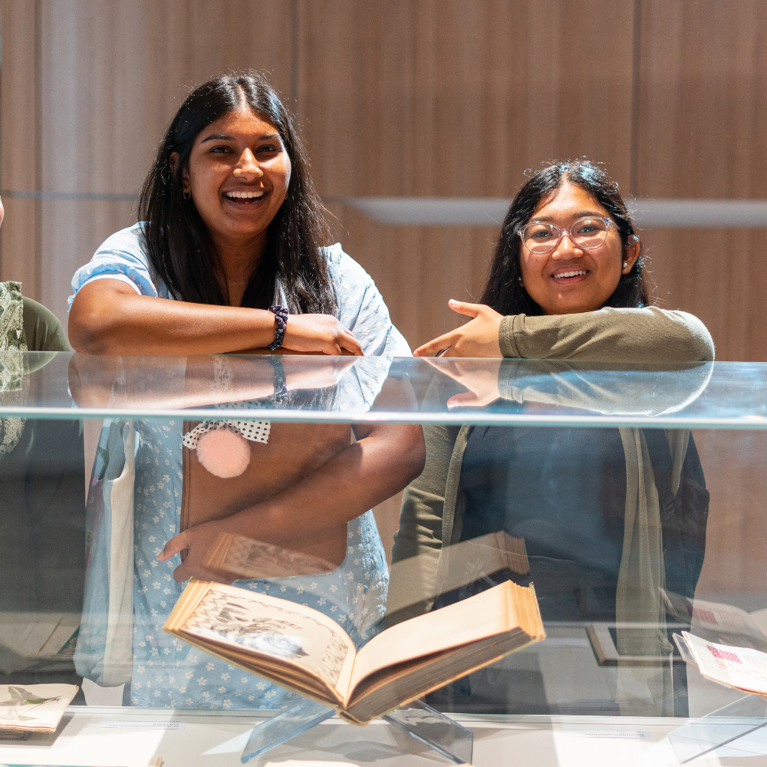 Image of four young students leaning on a glass case with a book in it