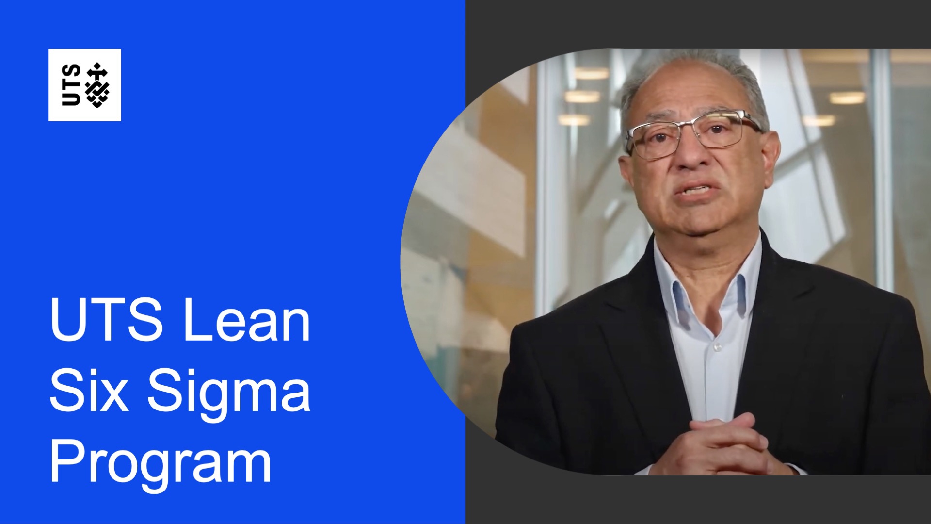 Mature male speaker in a suit, hands clasped, addressing the camera. Text reads 'UTS Lean Six Sigma Program' on a blue background. Professional setting.