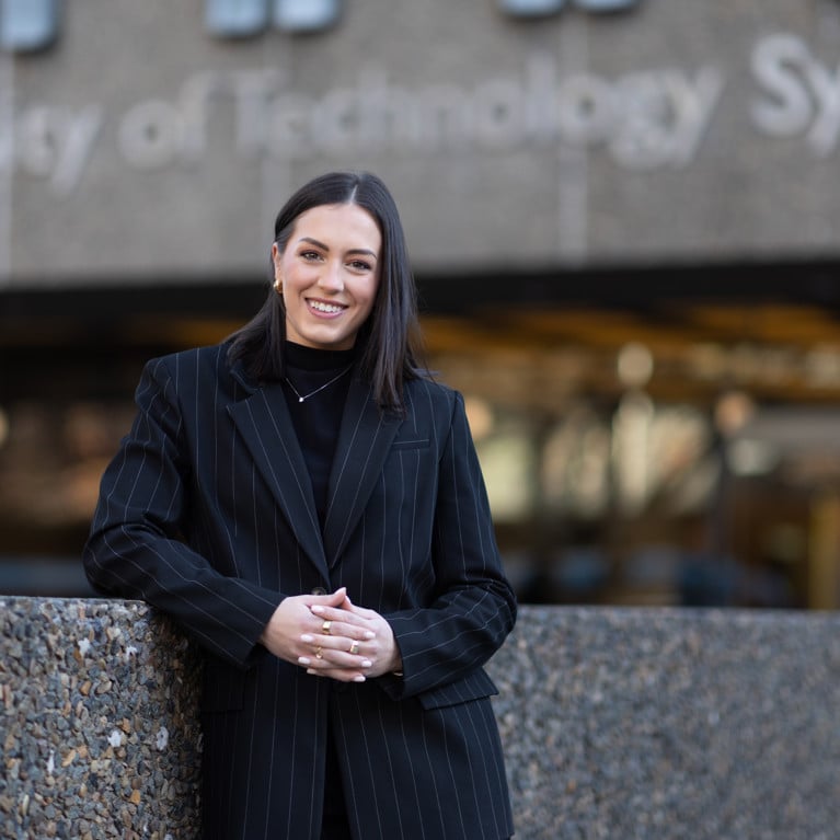 Georgia in a black pinstripe suit standing in front of UTS Building 1