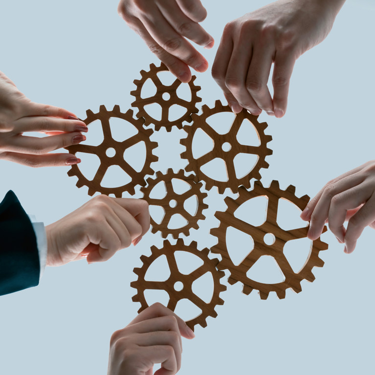 Hands holding wooden gears by businesspeople wearing suits for harmony synergy in office workplace concept. Picture: InfiniteFlow/Adobe Stock
