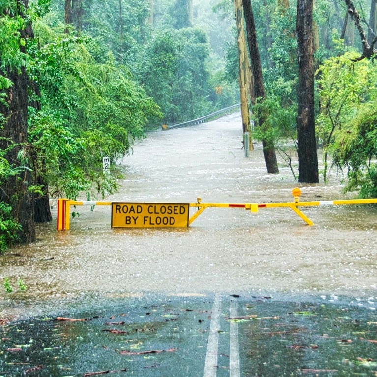 A flooded road in Australia surrounded by bushland, with a sign that reads: