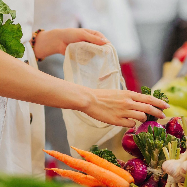 Female hands puts fruits and vegetables in cotton produce bag at food market