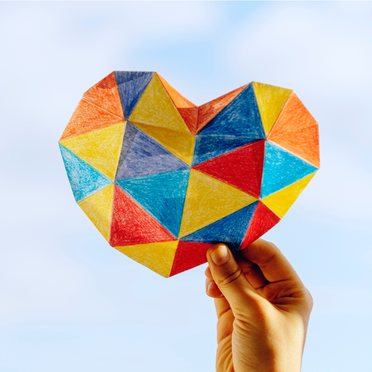 Hand holding up mutli-coloured paper heart.