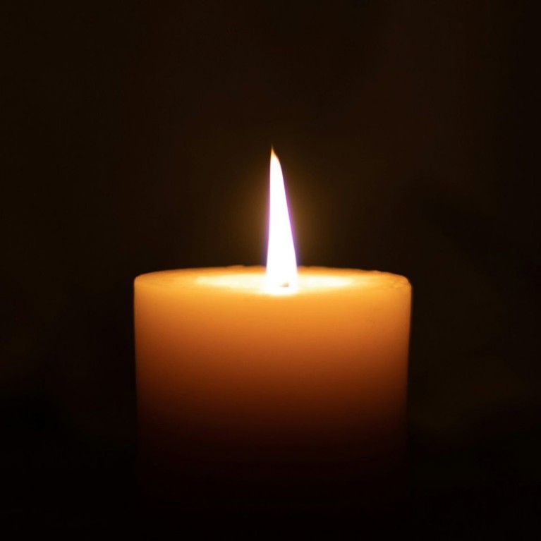 A lit candle burns in front of a dark background