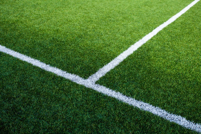Close-up of a sports field showing bright green artificial turf with two white boundary lines intersecting at a corner marking