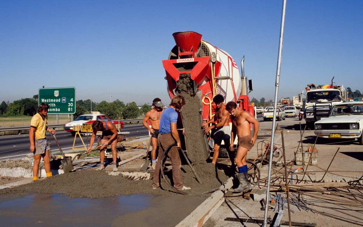 Australian workwear before hi-vis: DMR roadworkers at F4 Western Freeway Concreting Operations, between Granville and Parramatta, 1986, Department of Main Roads NSW, Transport for NSW historical image asset, file no #F4 DH 4 86 N15, State of New South Wales (Transport for NSW). Creative Commons Attribution 4.0 licence.