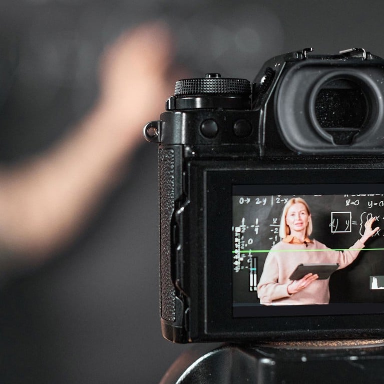 Teacher pointing at blackboard and recording lesson on professional camera