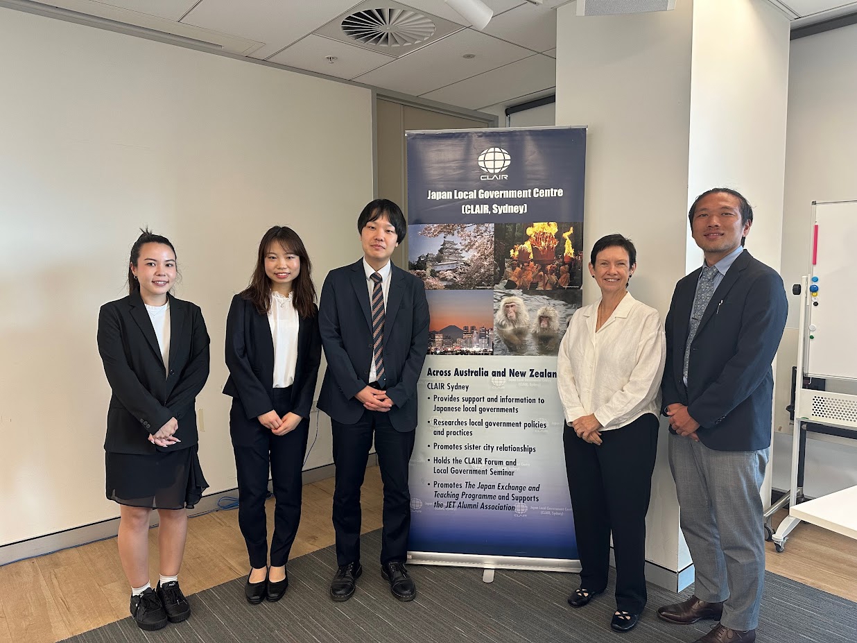 A photo of 5 people smiling and standing in front of a standing banner which reads "Japan Local Government Centre (CLAIR, Sydney)"
