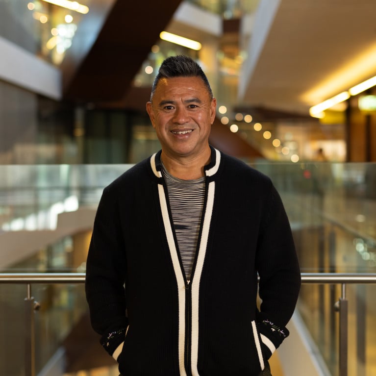 Troy Lum standing in a UTS building smiling and looking at the camera