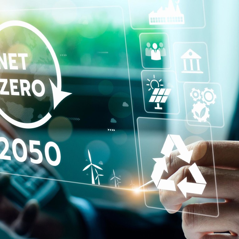 Man at laptop with pen and calculator in hand with Net zero by 2050 and a number of icons displaying on a screen