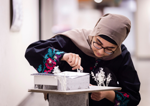 A woman focuses intently on assembling a model at her workspace.