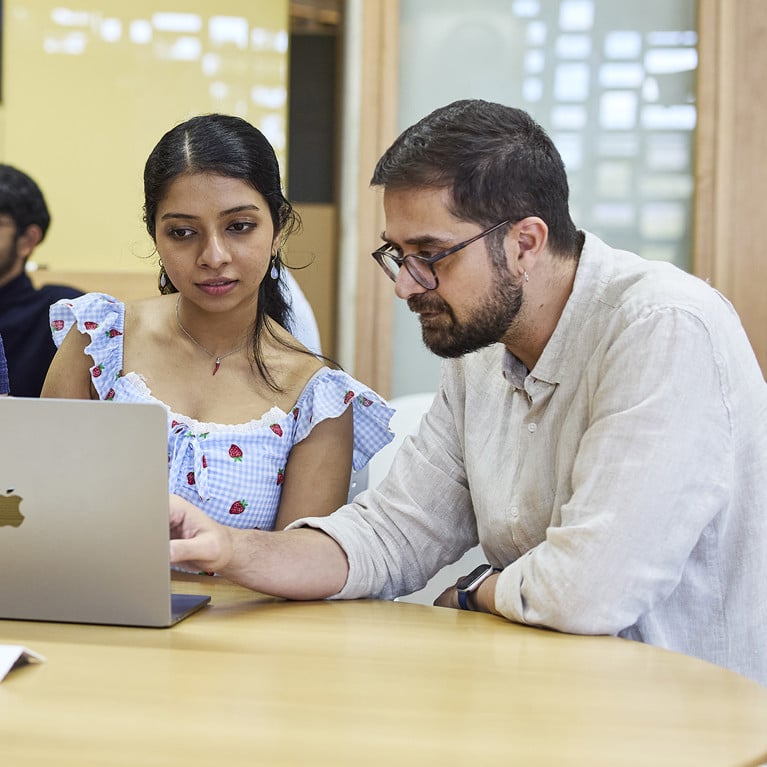 A diverse group of four people collaborates around a round table with laptops. They appear focused and engaged, creating a productive atmosphere.