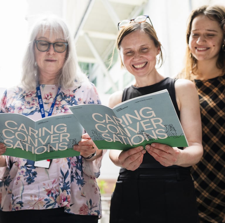 a group of females standing together reading a 'Caring Conversations' document