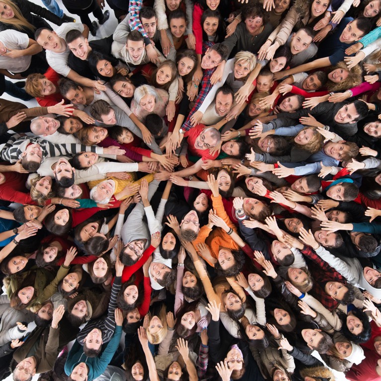 An aerial photograph of a crowd of people, looking up. They are all stretching their arms out into the centre of the group.