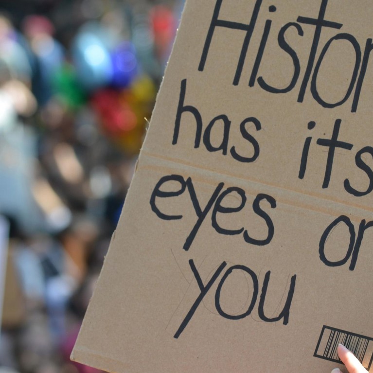 Sign saying ‘History has its eyes on you’ held up in a protest rally