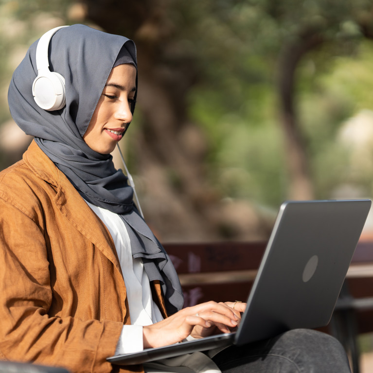 Young muslim woman sitting on a bench using a laptop