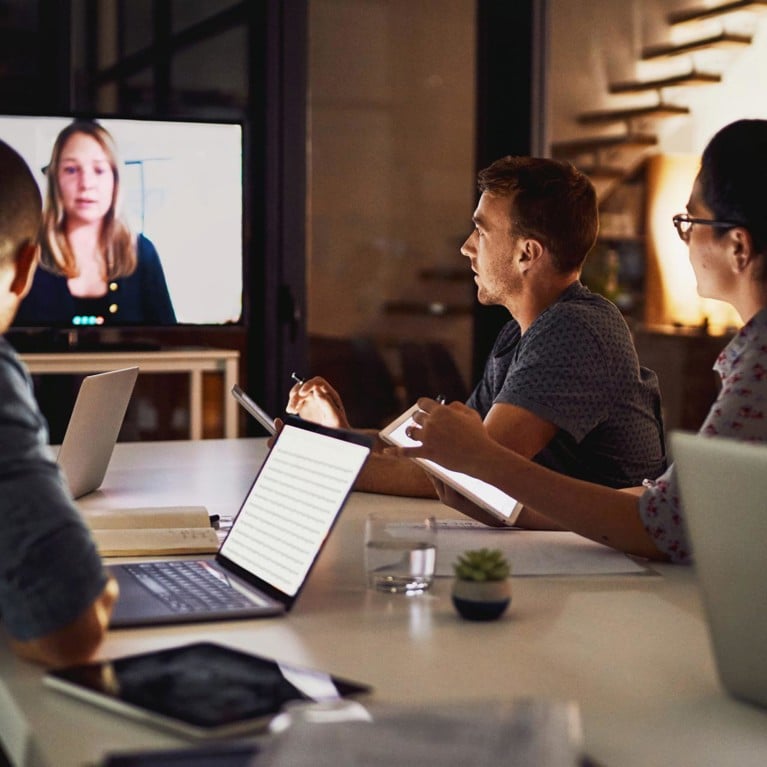 a group of colleagues sitting around a conference table and video conferencing with a person on a screen