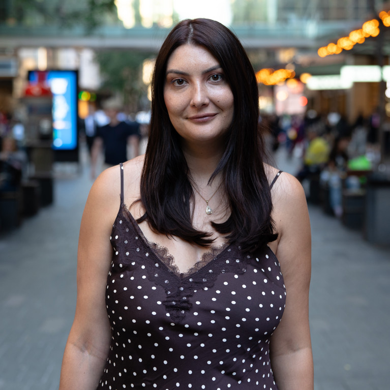 Portrait of Alison Gibson standing in a pedestrian precinct with people and city buildings blurred in the background.