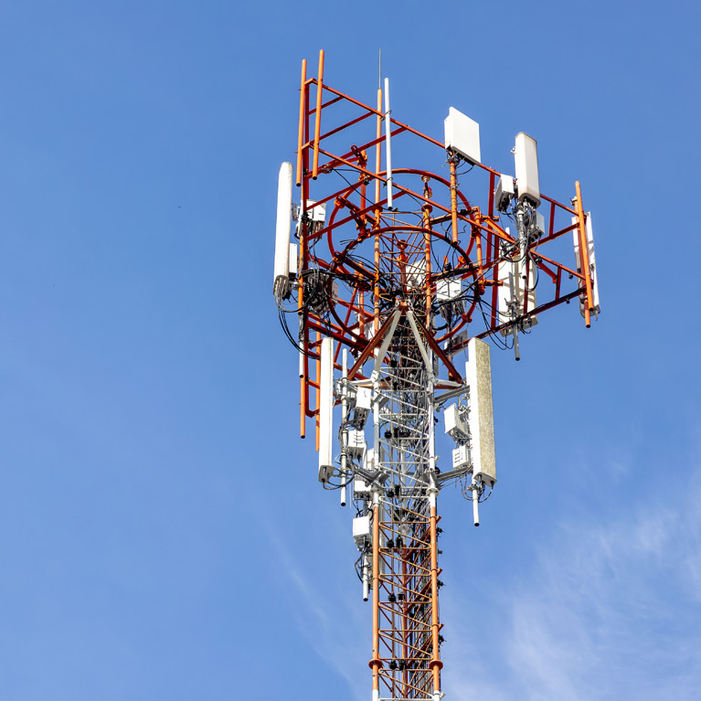 A telecommunications tower with antennas and satellite dishes stands against a clear blue sky, symbolising modern communication and connectivity.