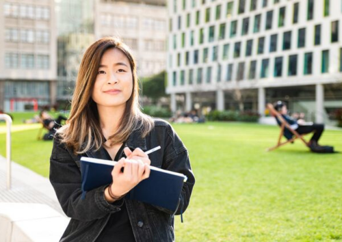 Student writing in a notebook while walking through the UTS Campus.