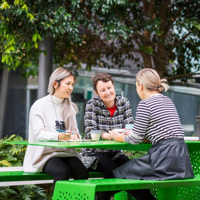 Three women sitting on outside seats at UTS's alumni green.