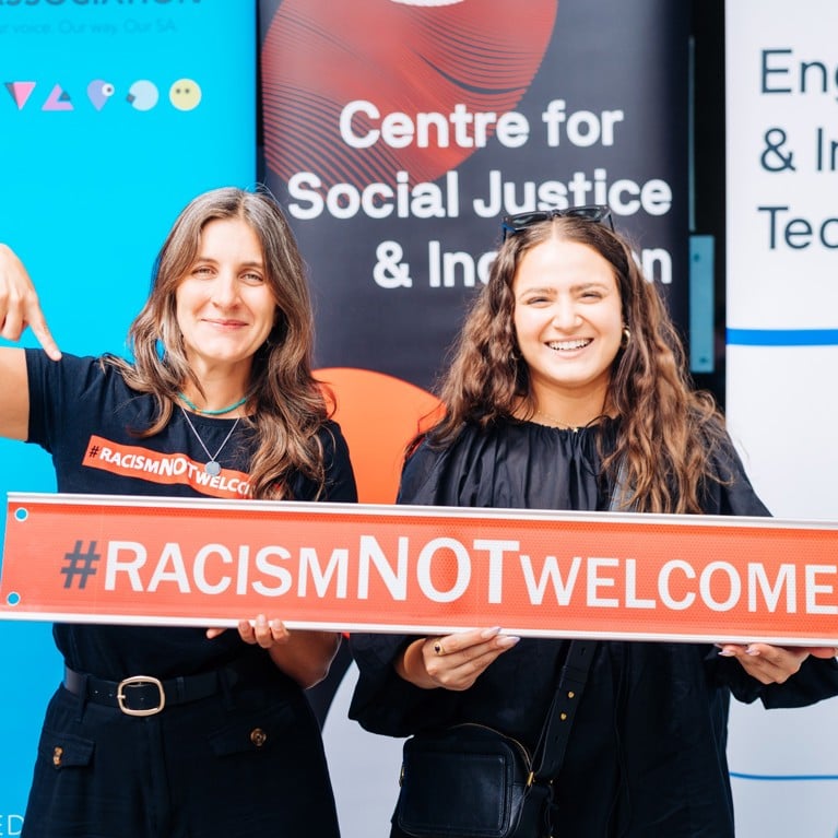 Two University of Technology Sydney staff members holding a 'Racism NOT Welcome' sign