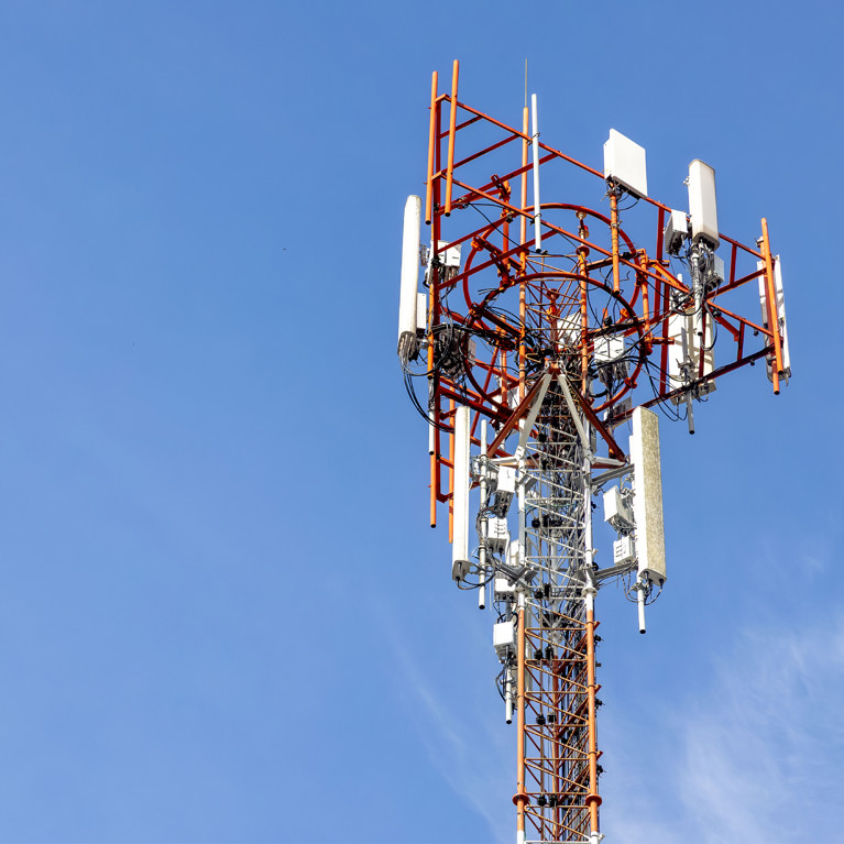 A telecommunications tower with antennas and satellite dishes stands against a clear blue sky, symbolising modern communication and connectivity.