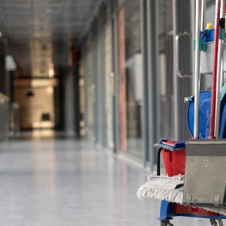 Cleaner pulling cleaning trolley down hallway