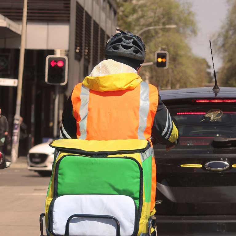 A food courier wearing hi vis clothing riding a motor bike in traffic. Picture by Rose Makin/Adobe Stock