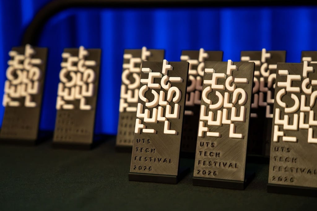 Image of trophies lined up in front of blue curtain. Trophies are a black rectangle shape with white 'Tech Fest' raised logo