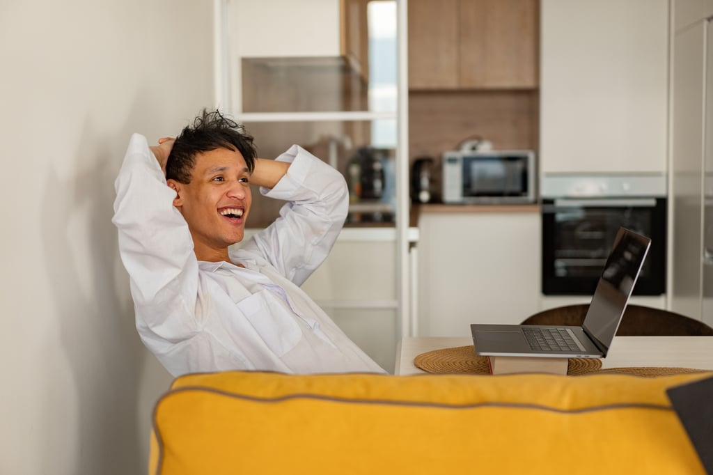 Student in their apartment studying at the dining table, smiling with their hands behind their head