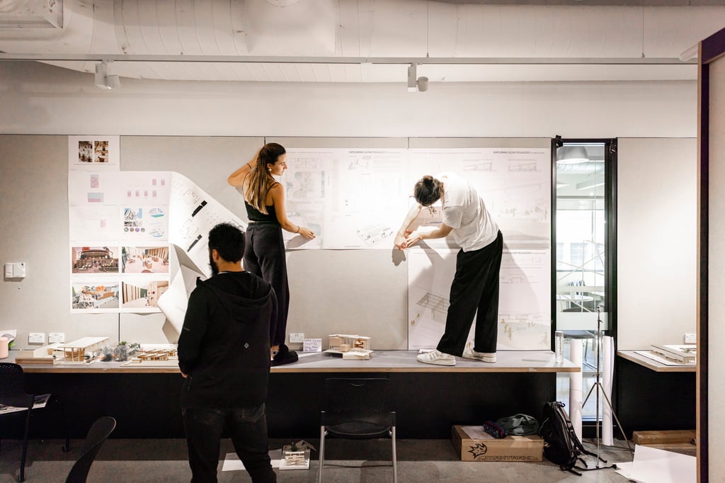 Architecture students stand on table sticking drafting drawings to the wall