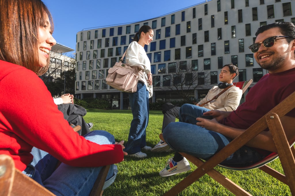 Group of students sitting on deck chairs on Alumni Green, smiling and talking.